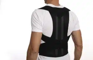 Rear view of a man wearing an adjustable black orthopedic posture corrector brace over a white t-shirt.