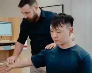 A male chiropractor checking a patient's extended arm for an elbow pain Chiropractor Singapore consultation.