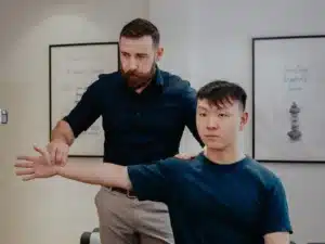 A patient's arm being assessed by a male doctor during an elbow pain Chiropractor Singapore appointment.