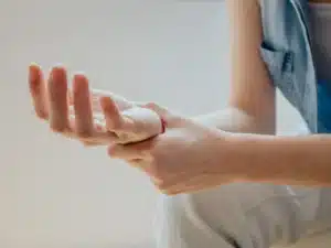 Close-up of a person sitting down and tenderly massaging or holding their wrist, indicating pain or discomfort in the hand and wrist joint.