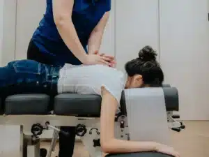A chiropractor applying manual pressure to the upper back of a female patient who is lying face down on a professional adjustment table.